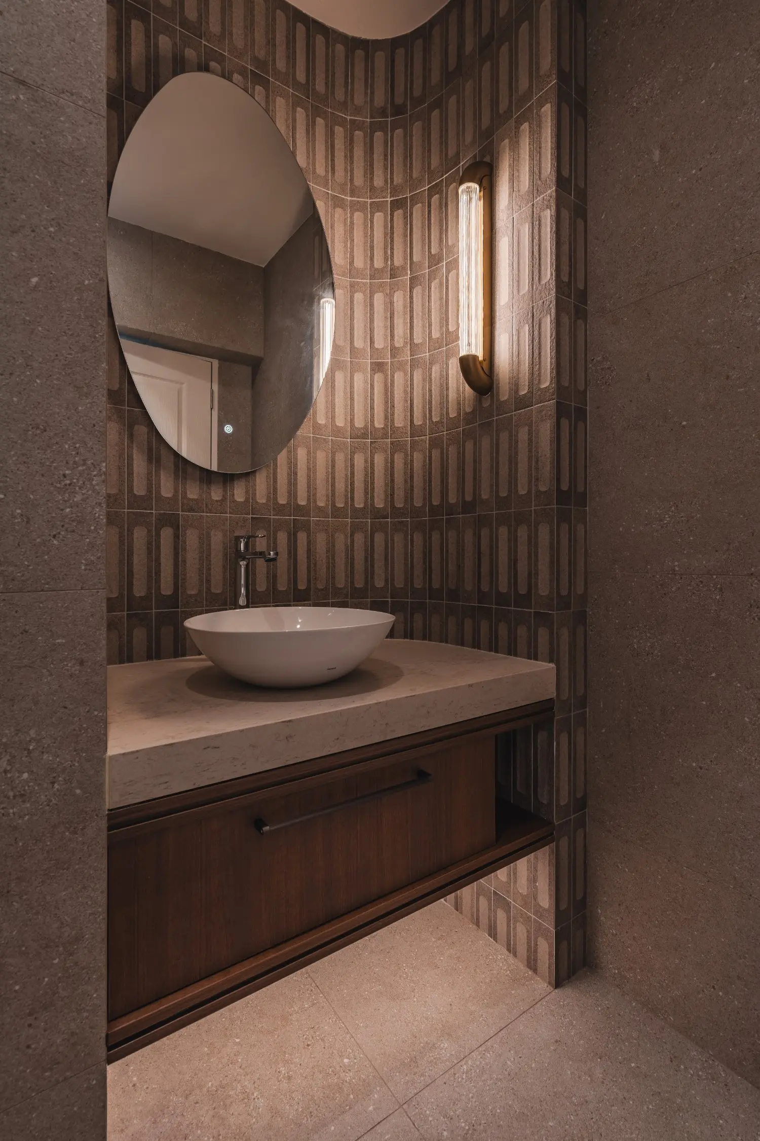 Bathroom vanity with curved mirror, textured tiles and warm lighting