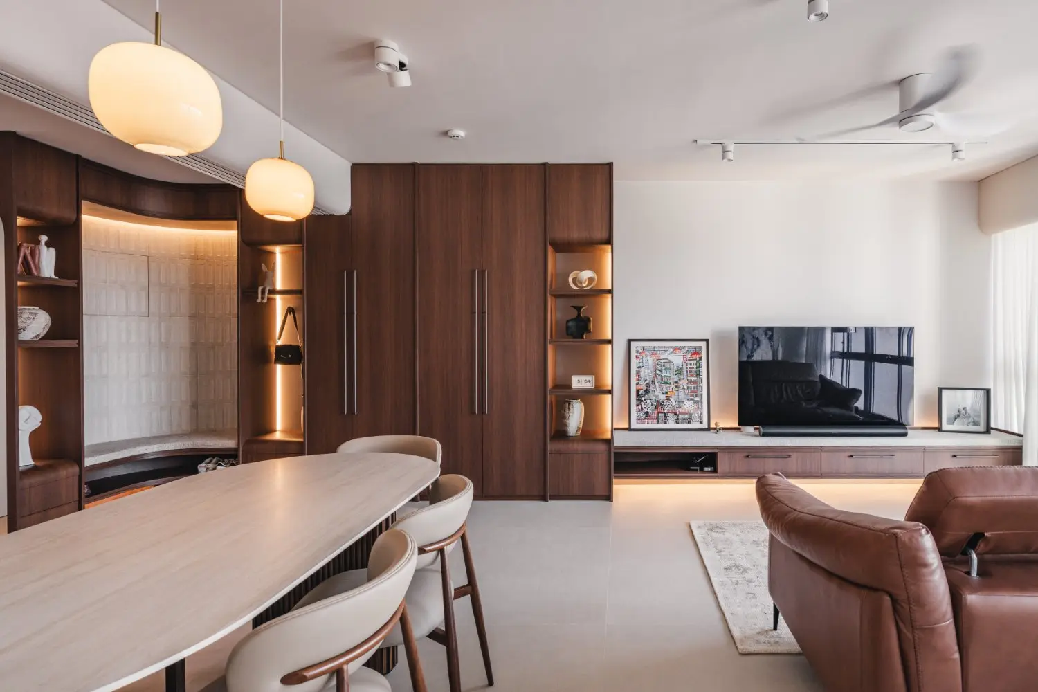 Rounded dining table facing the timber television wall and illuminated display joinery