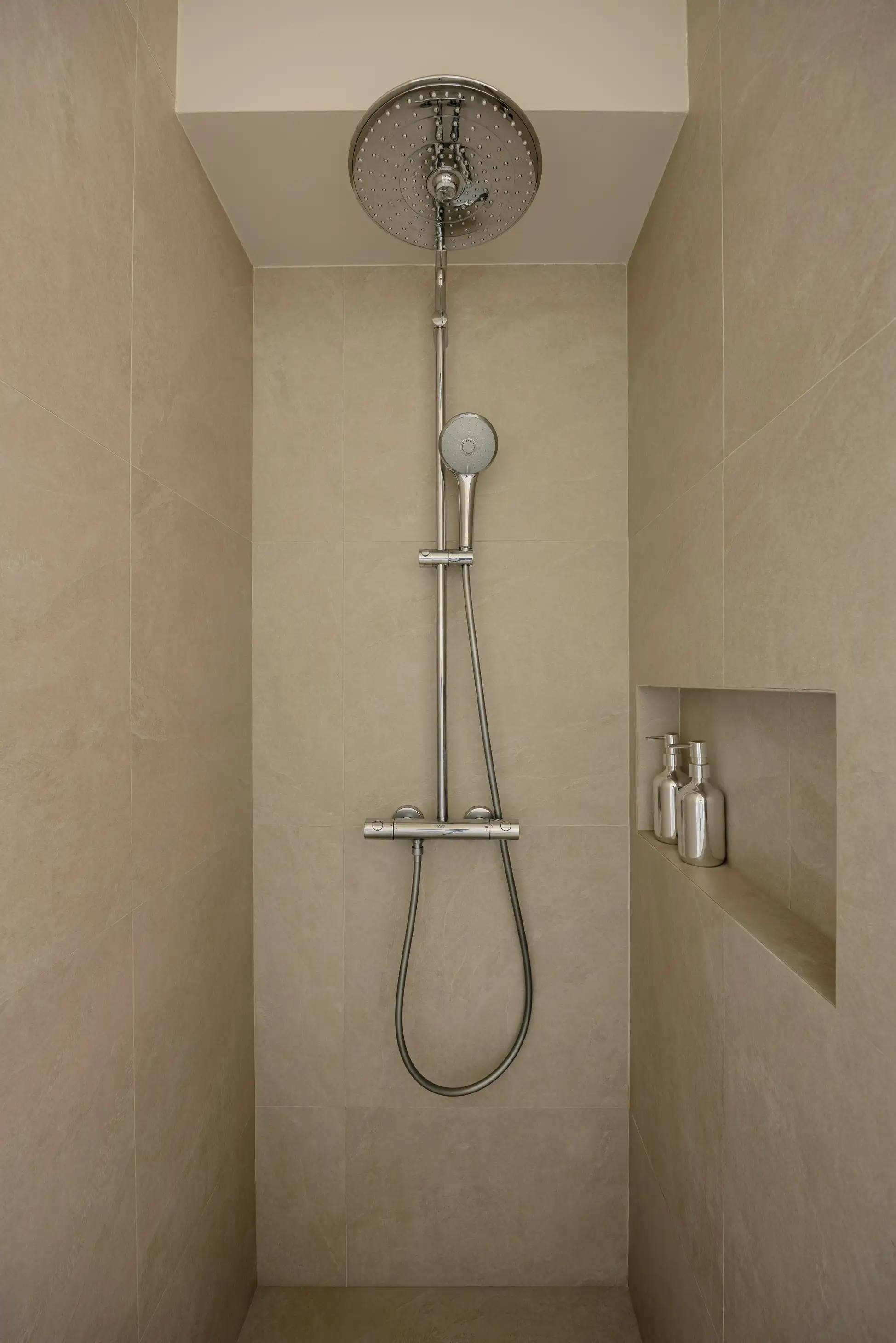 Minimal shower with large-format warm grey surfaces and recessed niche