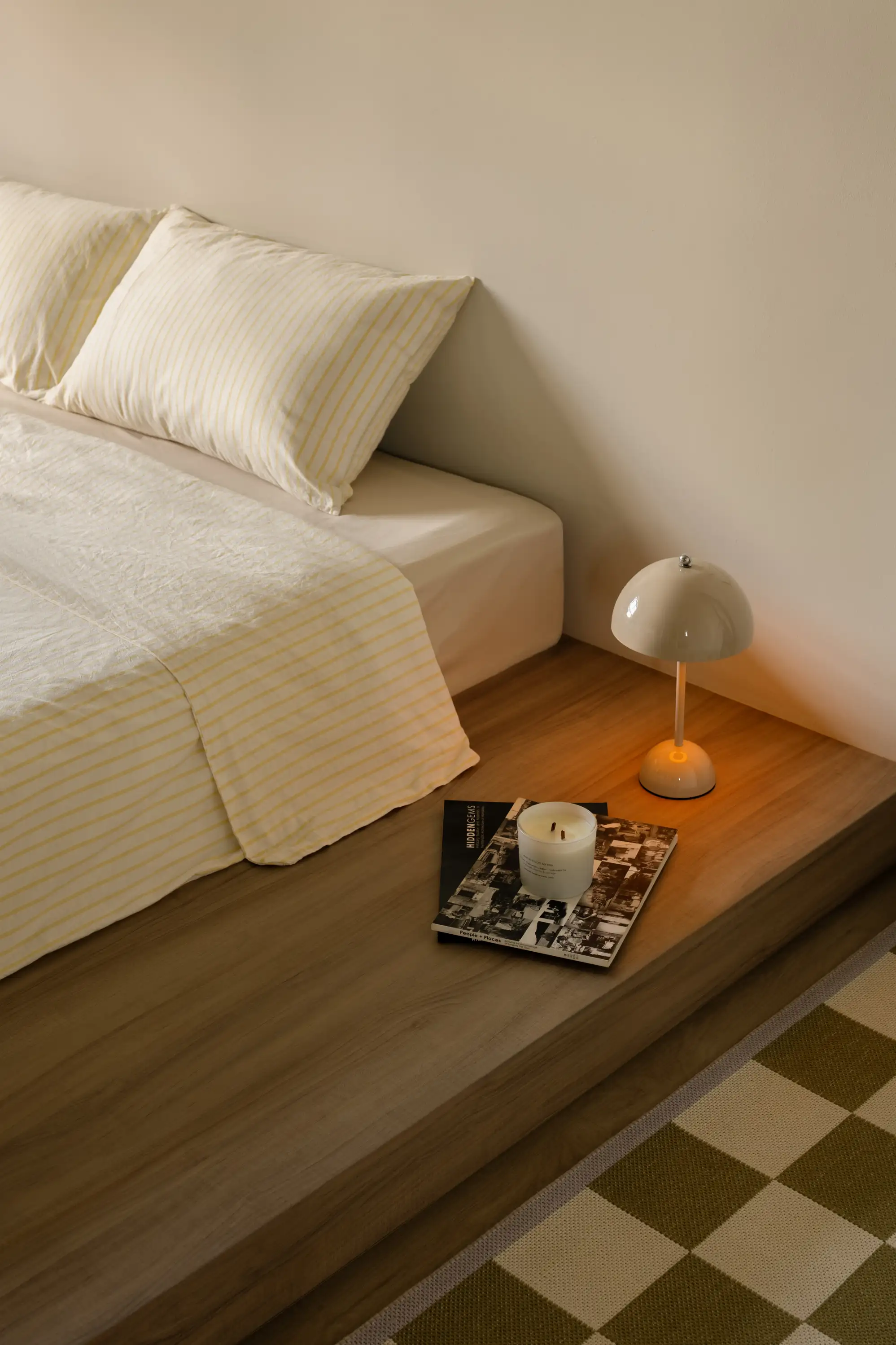 Bedroom corner with timber bedside ledge, sculptural lamp and checked flooring