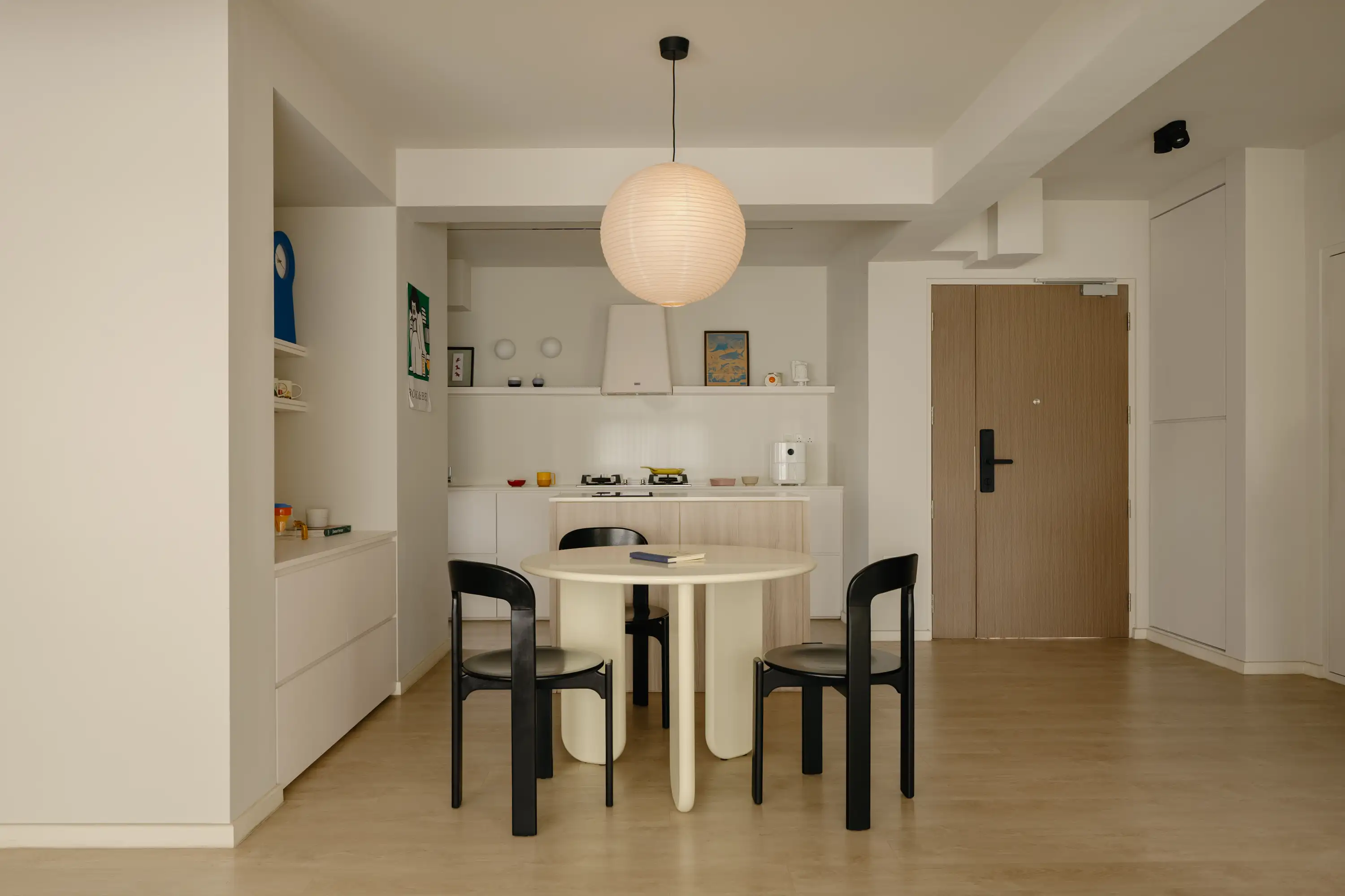 Round dining table with black chairs beneath a paper pendant
